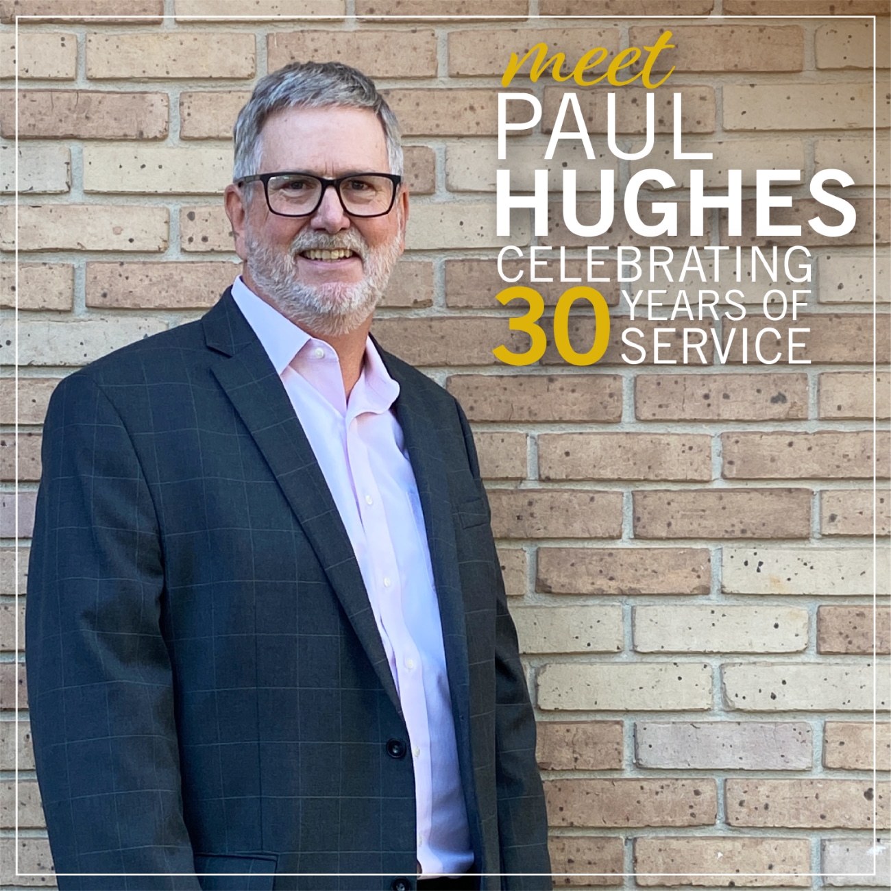 Paul Hughes in a dark suit and pink shirt smiling against a brick wall, celebrating 30 years of service at Greenville Federal Credit Union.