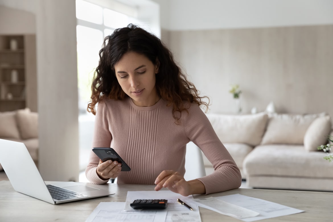 Woman using a phone and calculator to manage debt, illustrating tips to boost your credit score quickly.