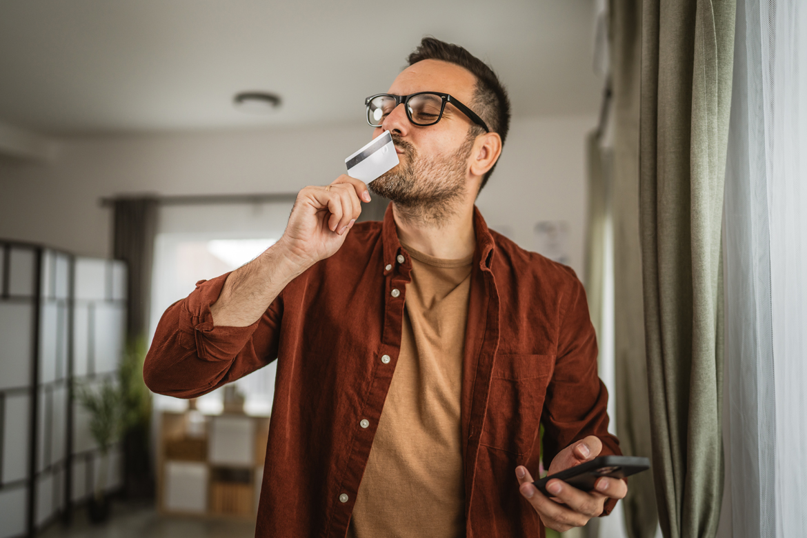 Man in orange shirt joyfully kisses credit card, symbolizing consolidation of credit card debt into one manageable loan.