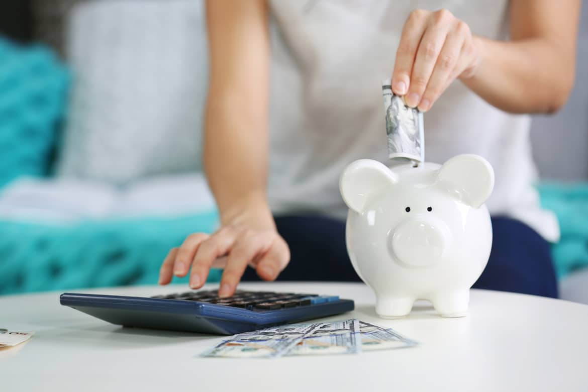Person saving money in a white piggy bank while calculating short-term savings accounts.