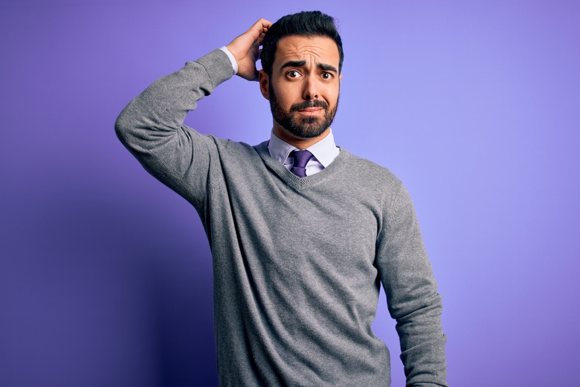 Confused man in gray sweater against purple background, pondering the difference between secured and unsecured debt.