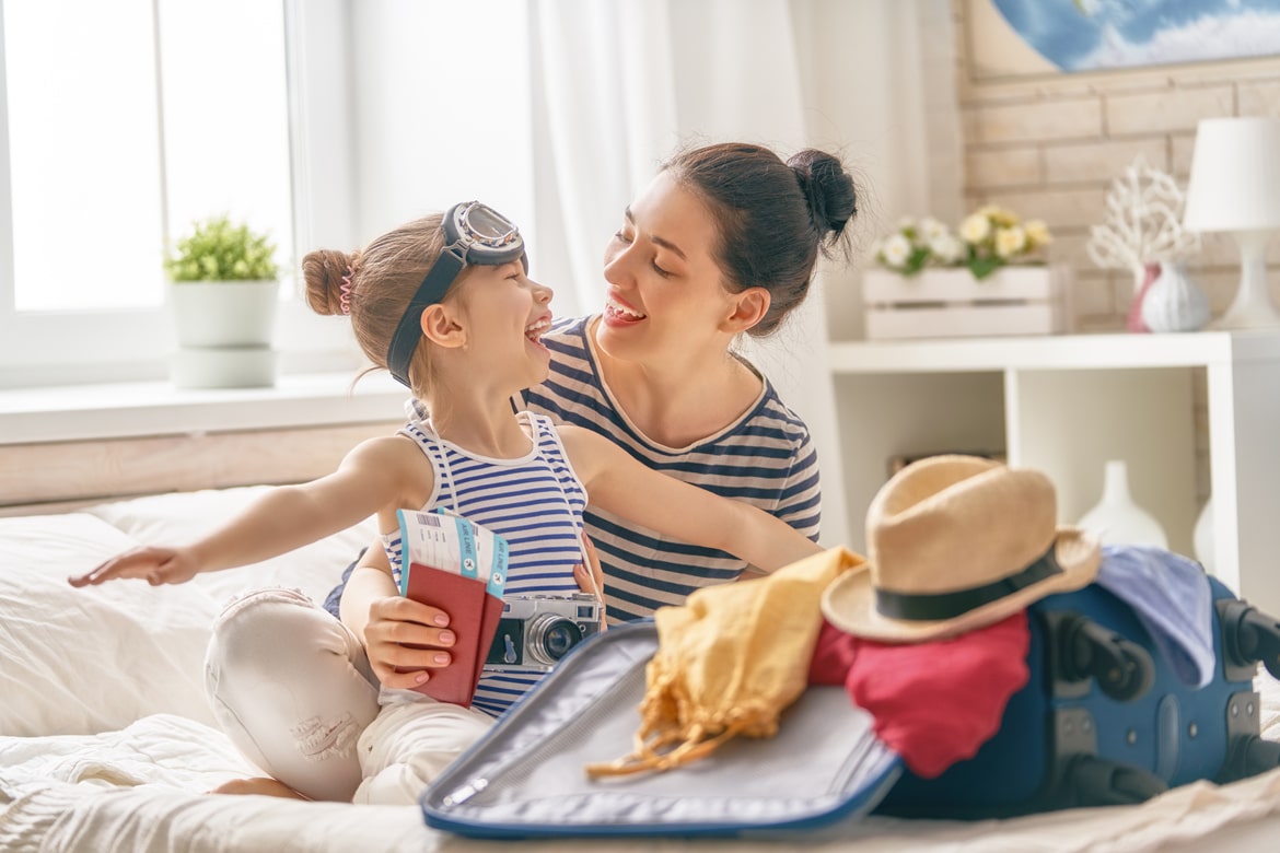 Mother and daughter packing suitcase for summer vacation, smiling, with tickets and passports, highlighting smart savings plans.