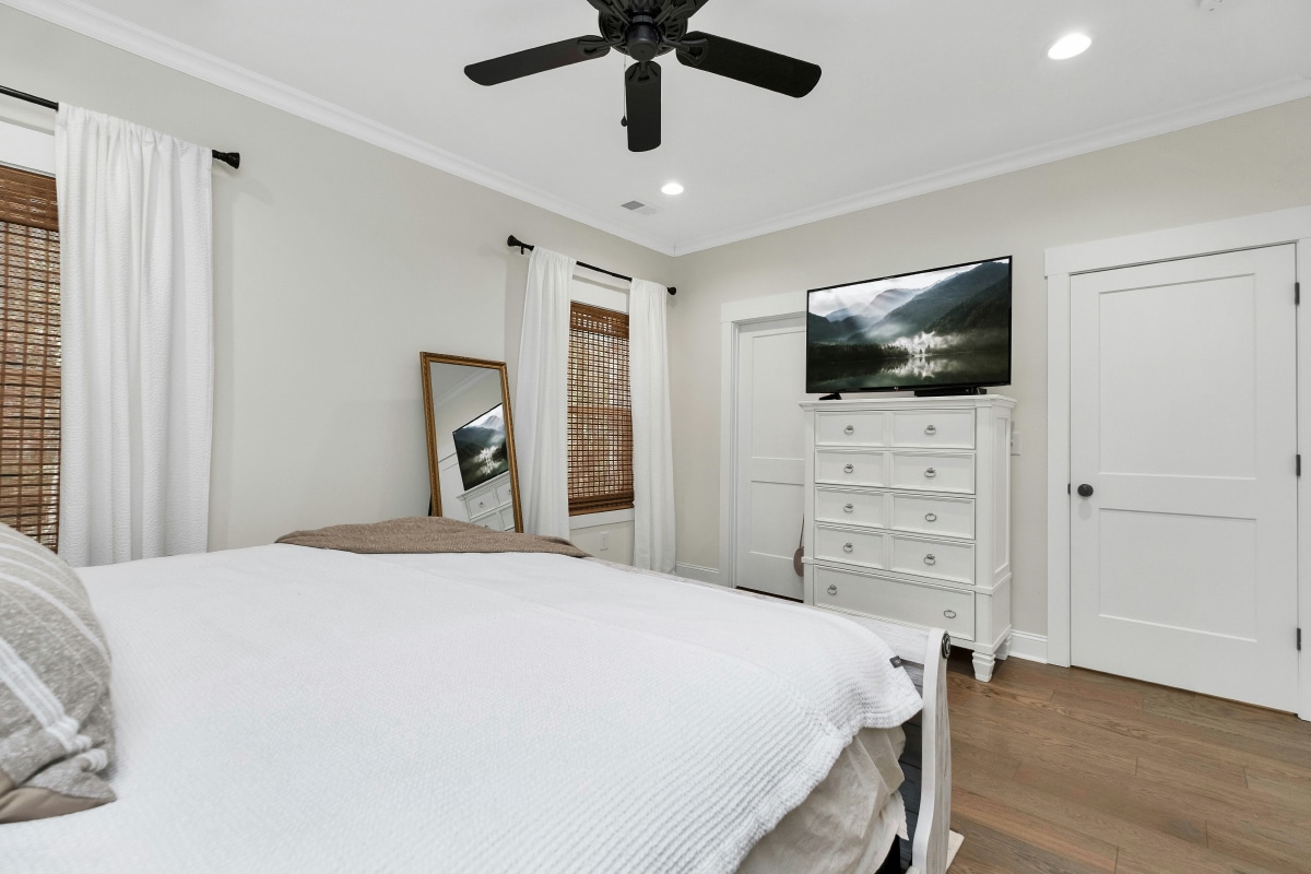 Bright bedroom with secure windows, ceiling fan, and organized dresser. Prepare your home before vacation.