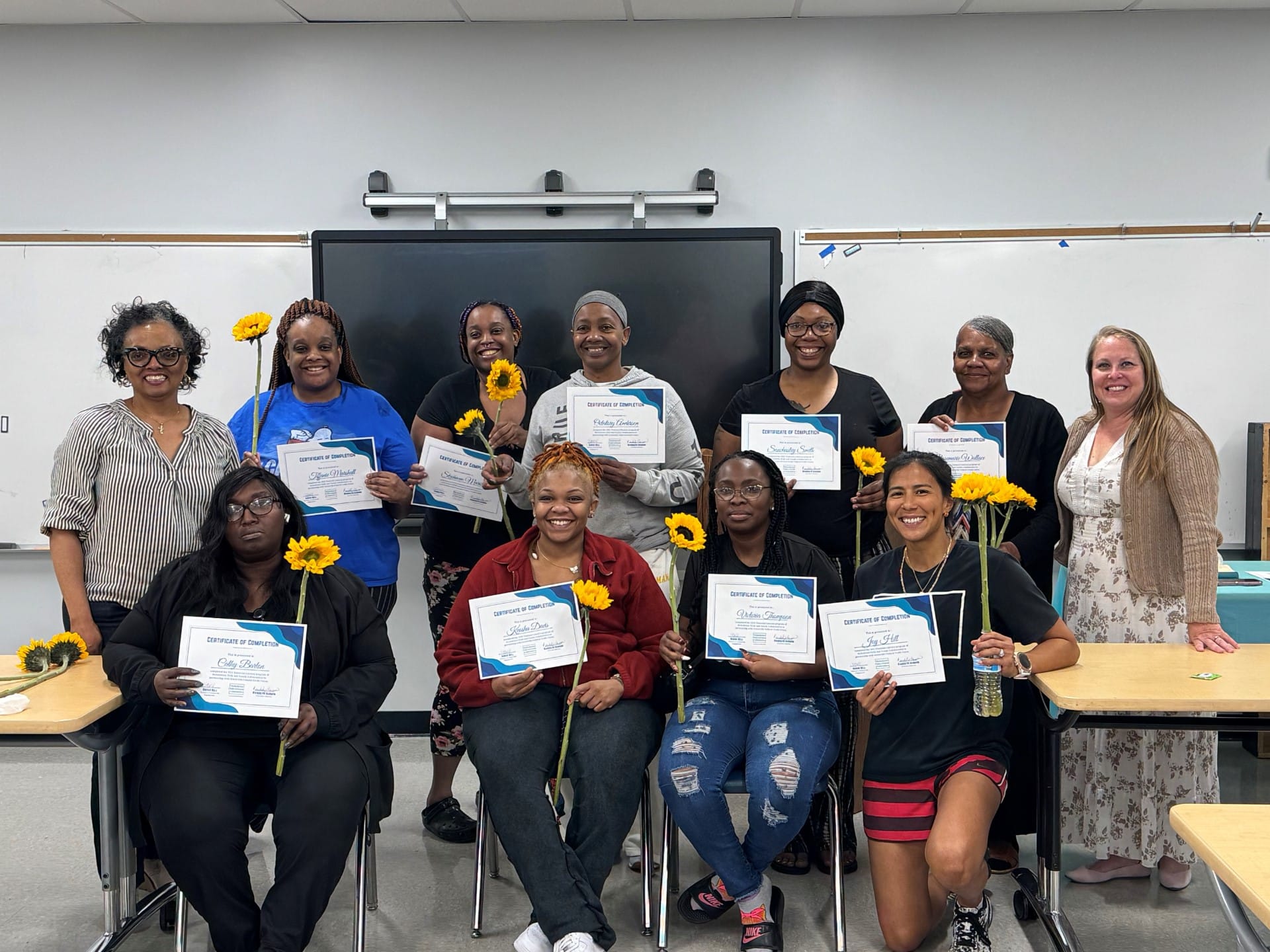 Nicholtown Child and Family Collaborative members proudly hold certificates and sunflowers, celebrating achievements in Greenville.