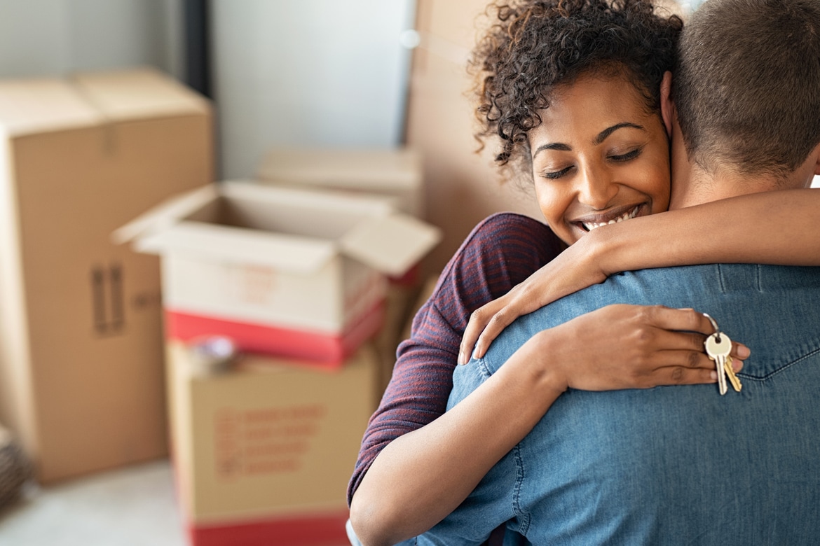 Happy couple embracing amid moving boxes, holding keys symbolizing new homeownership with adjustable-rate mortgages gaining traction due to lower initial rates.