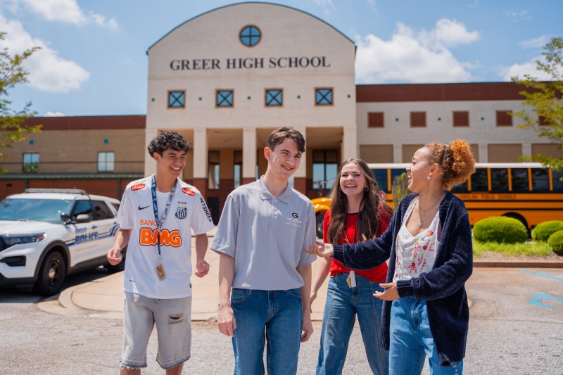 Greenville high school students laughing in front of their school, discussing new credit union student accounts.