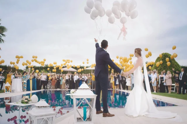 Wedding couple releases balloons by a pool, celebrating life events with guests, highlighting local personal loans.