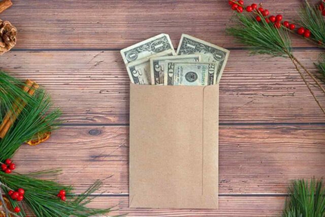 Envelope with cash surrounded by pine branches, symbolizing holiday savings with Greenville Federal Credit Union.