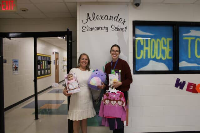 Two women at Alexander Elementary School holding donated toys and clothes, exemplifying Greenville Federal Credit Union's community impact through local partnerships.