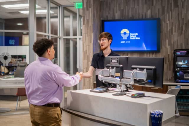 Customer and employee shaking hands at a credit union counter, highlighting core values and personal banking.