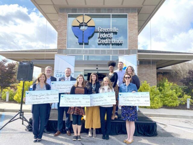 Group holding oversized checks in front of Greenville Federal Credit Union, showcasing foundation funds and grants for education empowerment.