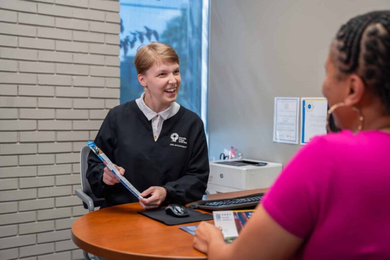 smiling woman showing a pamphlet while sitting at a desk