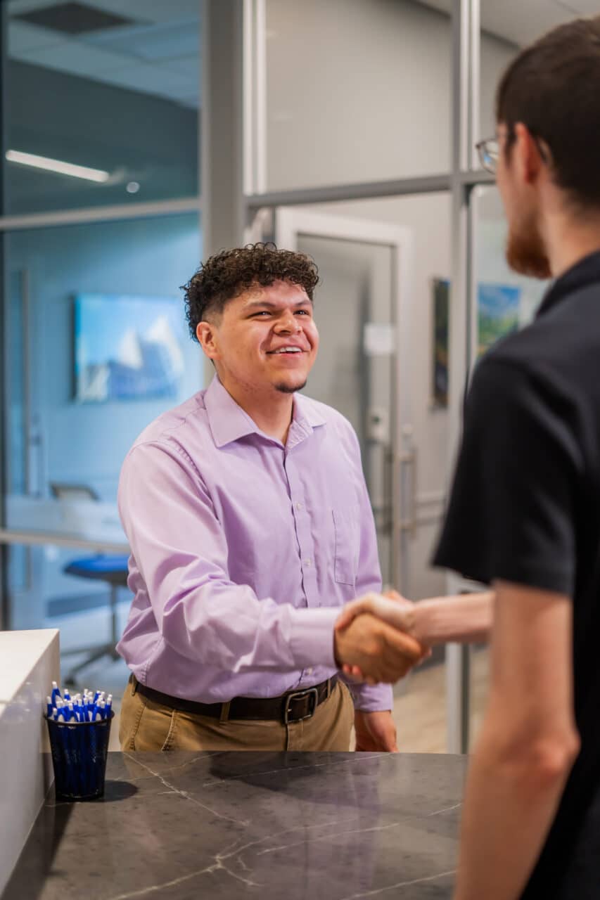 Man in a purple shirt shaking hands with a visitor in a modern office setting, promoting Greenville Federal Credit Union.