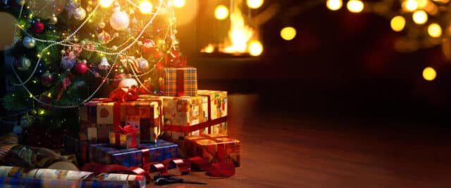 Christmas tree with ornaments and wrapped presents by a cozy fireplace, highlighting holiday savings for vacations.