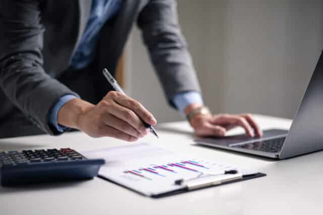 Businessman reviews financial charts on laptop, enhancing payables solutions and business efficiency with ACH origination.