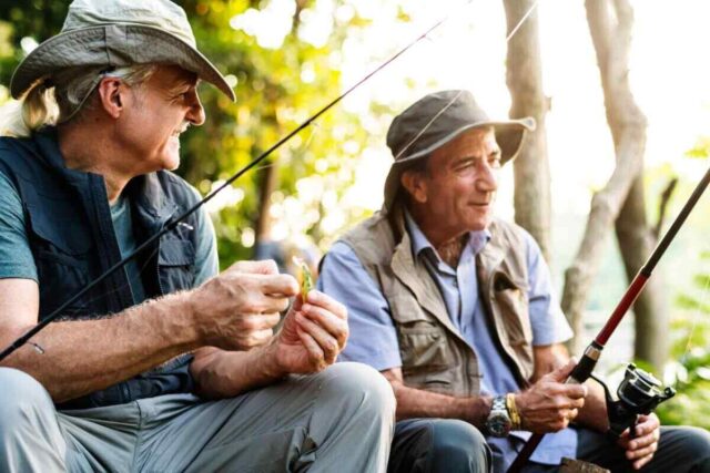 Senior friends fishing by a sunlit lake, wearing hats and vests, symbolizing flexible Roth IRA growth.