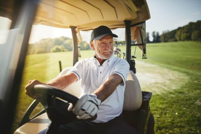 Senior man smiling while driving a golf cart on a sunny course, illustrating the flexible lifestyle Roth IRAs offer.