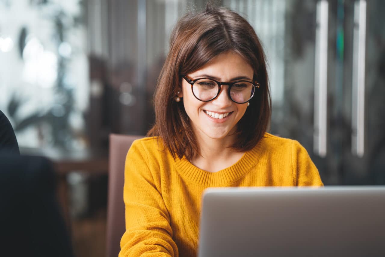 Smiling businesswoman in glasses working on laptop, representing Greenville Federal Credit Union's tailored credit offers.