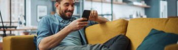 Man relaxing on sofa, using smartphone to access online bill pay steps and manage payees in cozy living room.