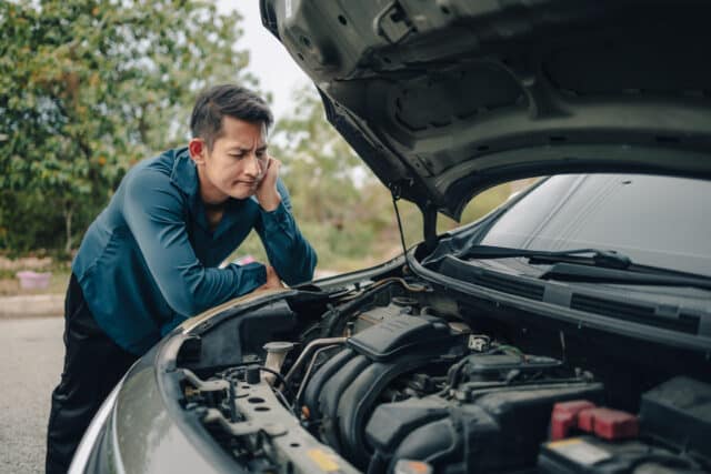 Man looks at car engine on roadside, contemplating loan insurance to protect finances and coverage options.
