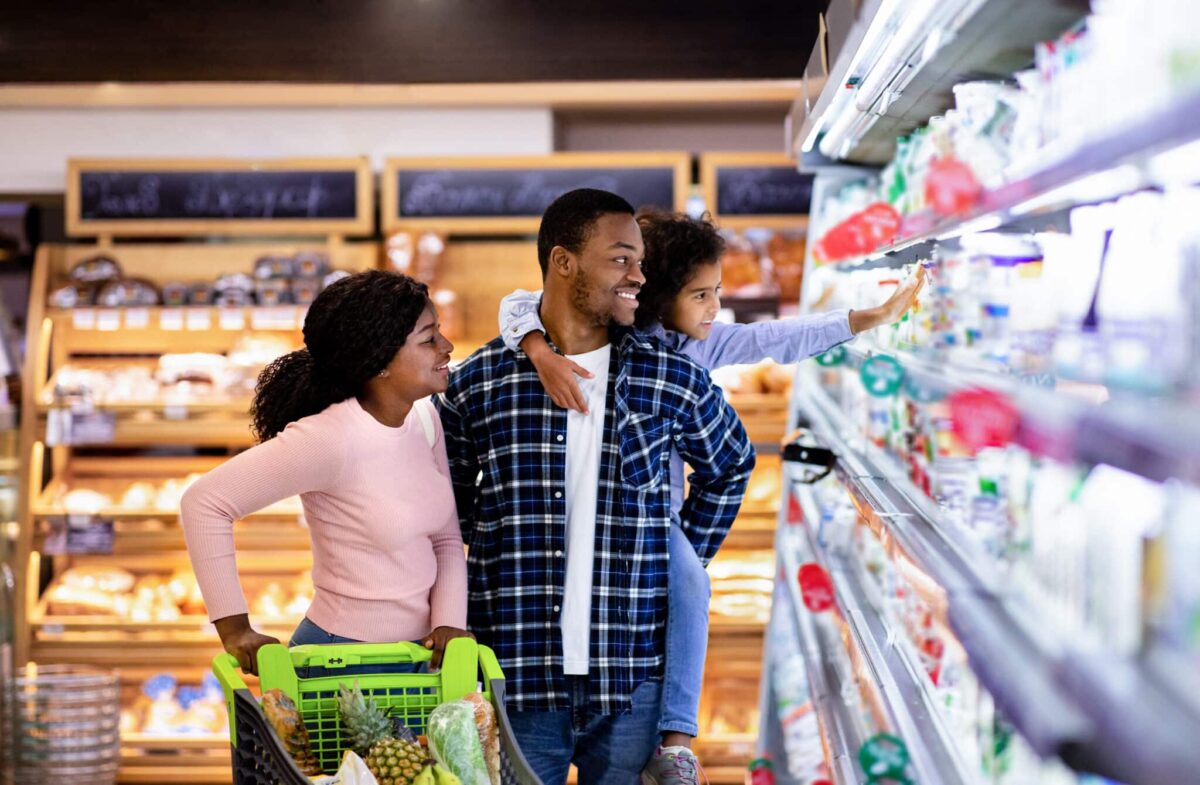 Happy family shopping in grocery store, choosing milk; unlock premium rewards with Greenville Visa Signature.