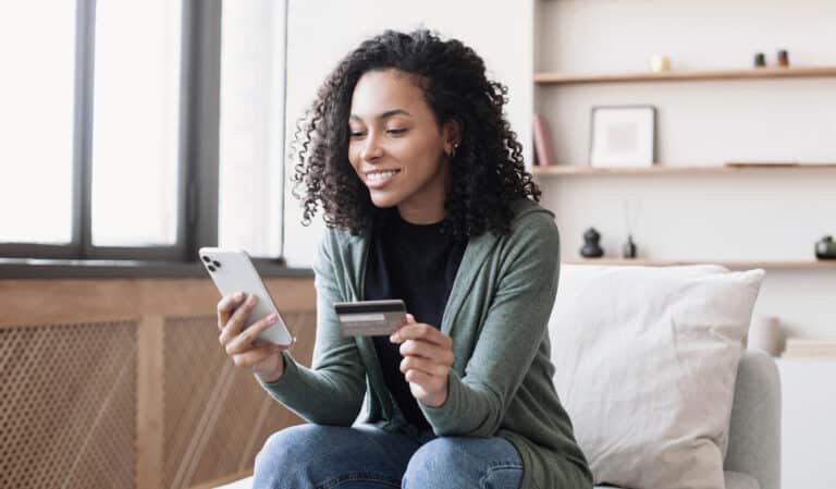 Woman using smartphone and holding credit card, conducting online banking securely at home.