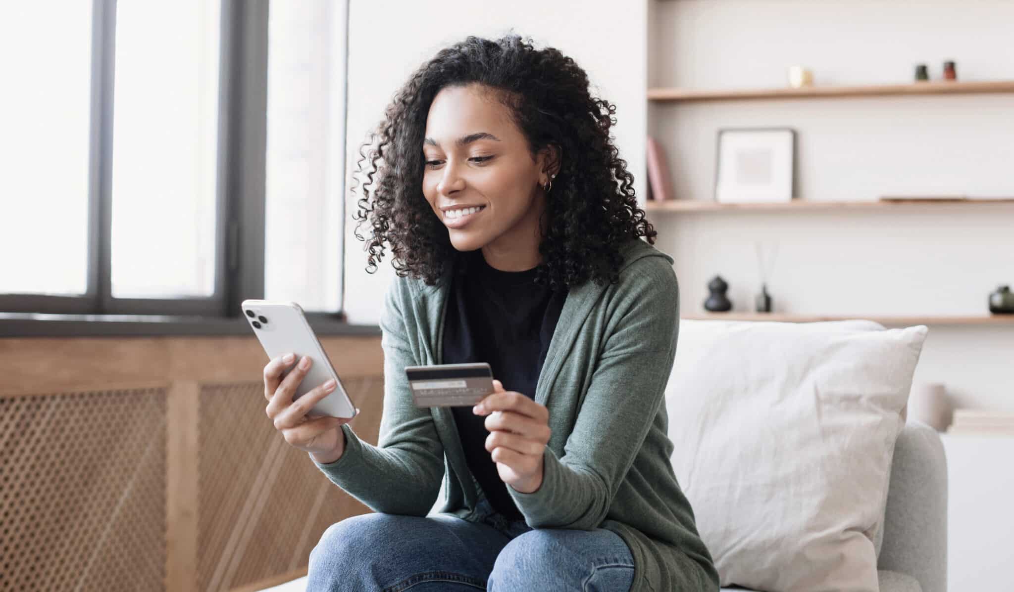Woman using smartphone and holding credit card, conducting online banking securely at home.