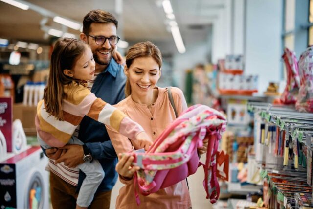 Family shopping for a pink school backpack, smiling happily in store aisle. Unlock premium rewards with Visa Signature.