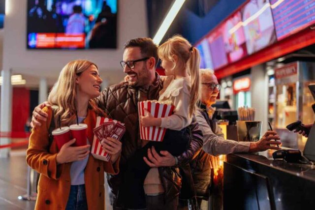 Happy family in bright coats buys popcorn and drinks at cinema, enjoying rewards from Kasasa Cash Checking.