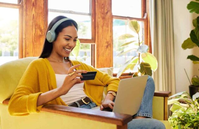 Woman in a yellow sweater enjoying online shopping and music, considering investing in share term certificates.