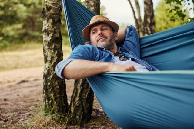 Man in a hat relaxes in a hammock, symbolizing the ease and benefits of Yield Plus Savings with higher interest.