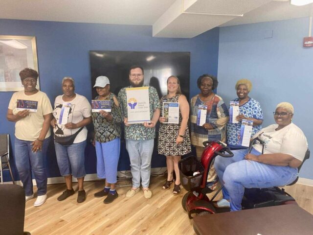 Greenville Federal Credit Union team promotes Company Partner Program, holding brochures for customized services.