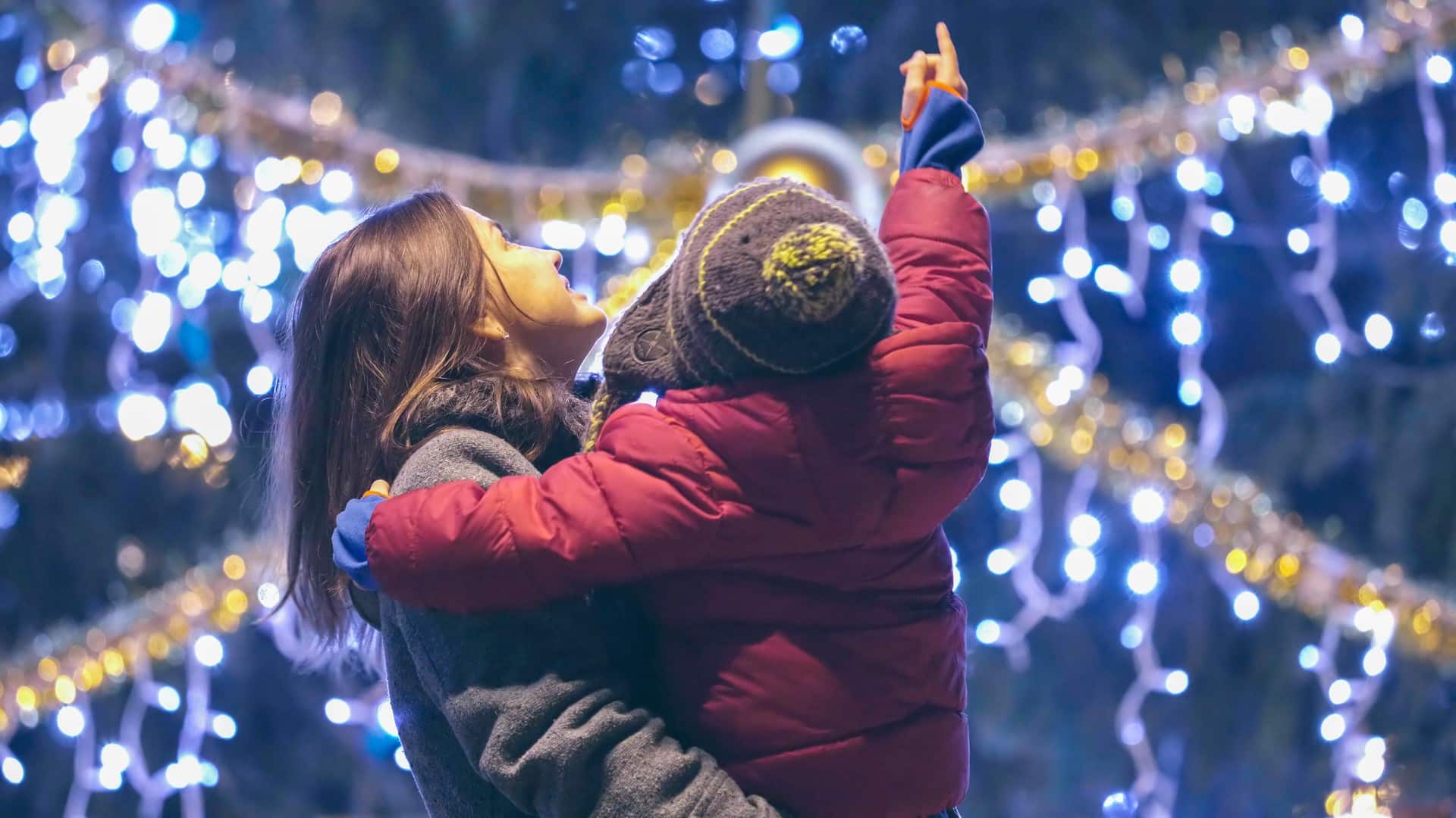 Mother and child in winter clothes admire twinkling holiday lights, enjoying affordable festive fun in Greenville.