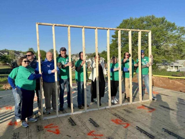Team members in green shirts raise a wooden frame at a Greenville Federal Credit Union community build.
