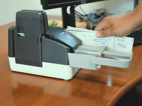 Hand using remote deposit capture machine to digitally process checks, streamlining receivables and payment services.