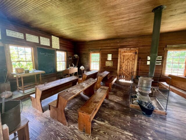 Rustic wooden classroom with benches, a potbelly stove, and instructional charts. Greenville FCU members enjoy exclusive discounts.