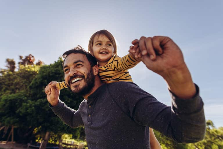 Father carrying child on his back outdoors, embodying community and commitment to flexible family moments.