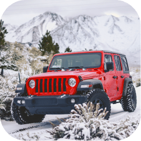 Red SUV driving through snowy mountain landscape, showcasing Greenville Federal Credit Union's competitive vehicle loans.