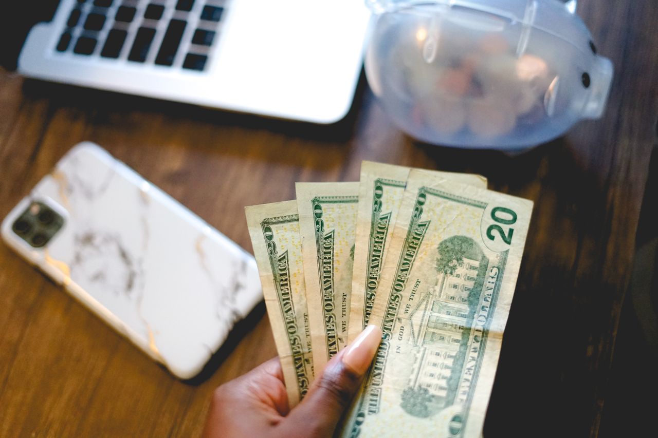 woman holding money with phone and computer
